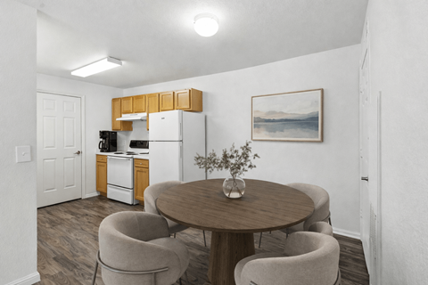 A kitchen with a refrigerator, a dining table with chairs, and a painting on the wall.