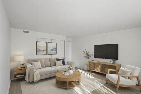A living room with a grey couch, a wooden coffee table, a white chair, and a black television mounted on the wall.