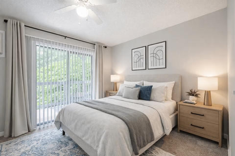 A bedroom with a large bed, a ceiling fan, and a view of the outdoors through the window.