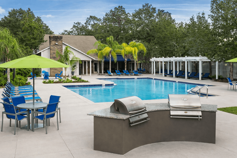 A pool with a table and chairs and a sun shade. at Parkland at Orange Park Apartments , Orange Park