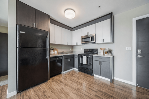 A black refrigerator is in a kitchen with wooden floors.