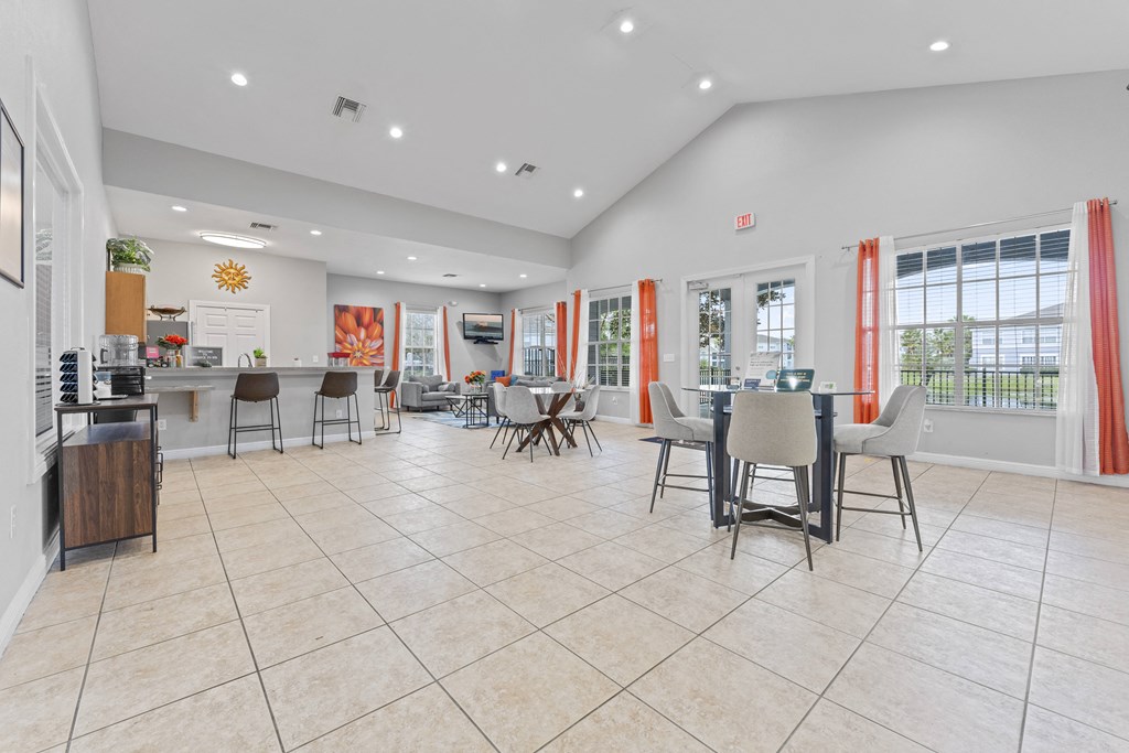 a dining area with tables and chairs and a kitchen with a counter and windows