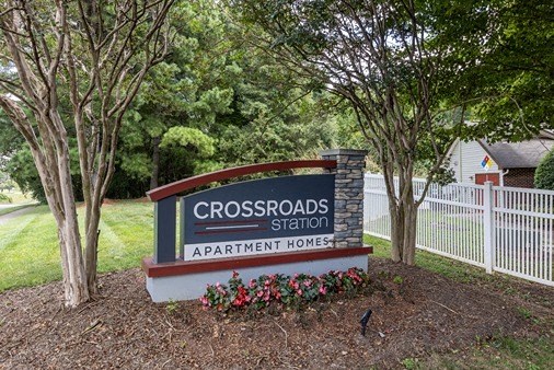 a sign for the crossroads station in front of a fence and trees