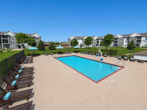 A swimming pool surrounded by sun loungers and umbrellas in a residential area.