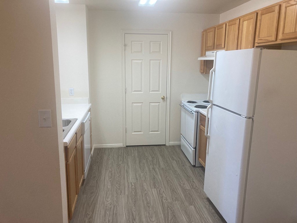 an empty kitchen with white appliances and wood floors