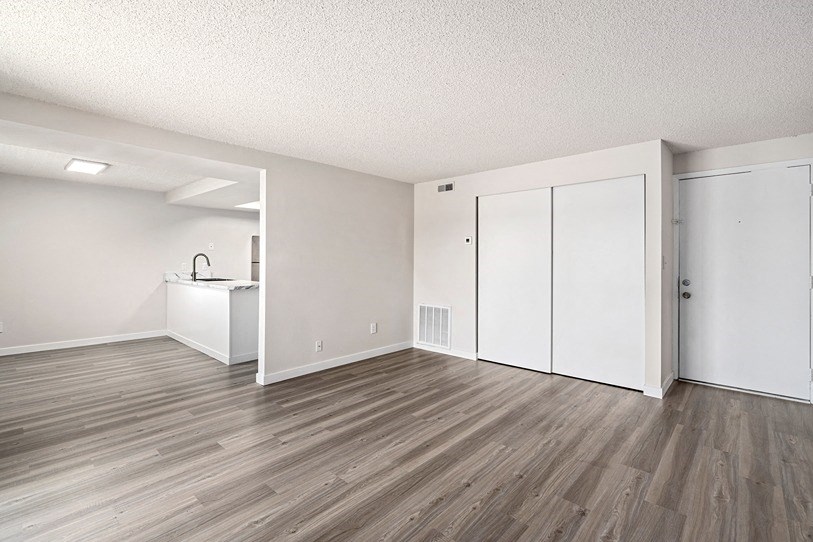 an empty living room with a kitchen in the background
