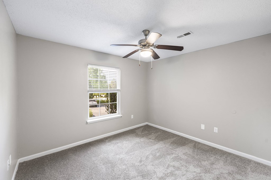 an empty bedroom with a ceiling fan and a window