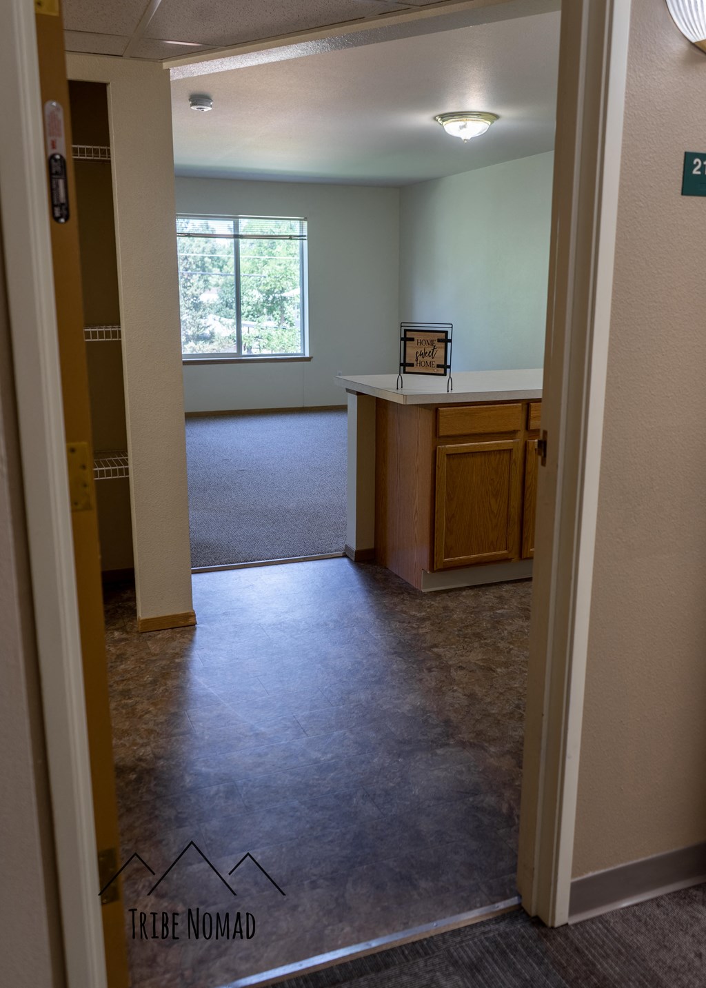 an empty living room with a kitchen and a window