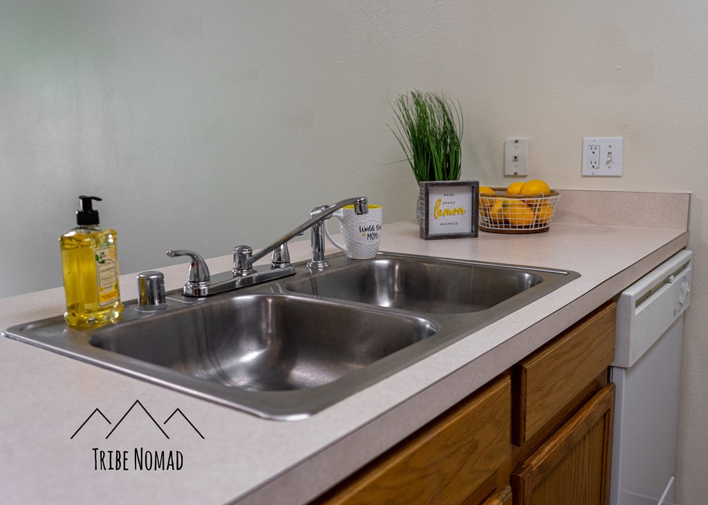 a kitchen sink with a white counter top and wooden cabinets