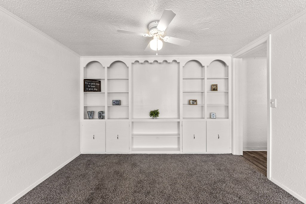 a living room with white shelves and a ceiling fan