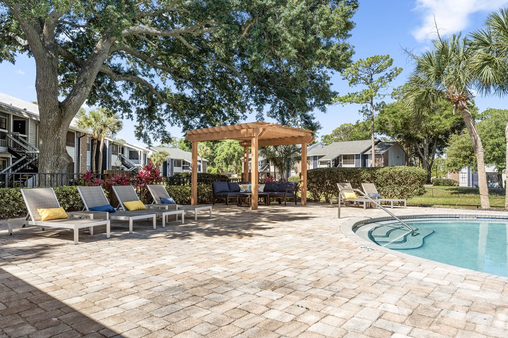 a backyard with a pool and patio with chairs and a gazebo