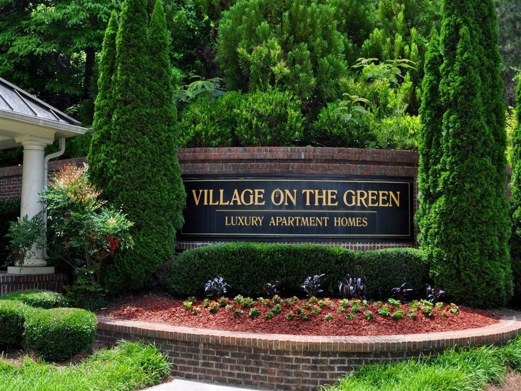 a sign for village on the green in front of trees
