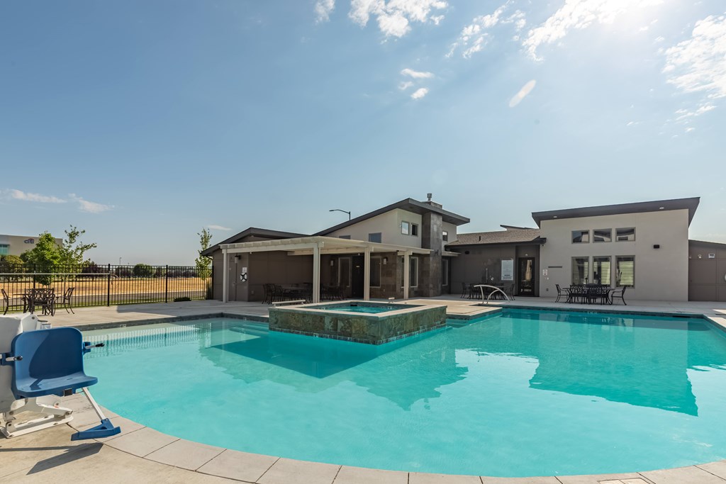 A swimming pool in front of a house with a sunny sky. at Harper Ridge Apartments, Meridian, Idaho