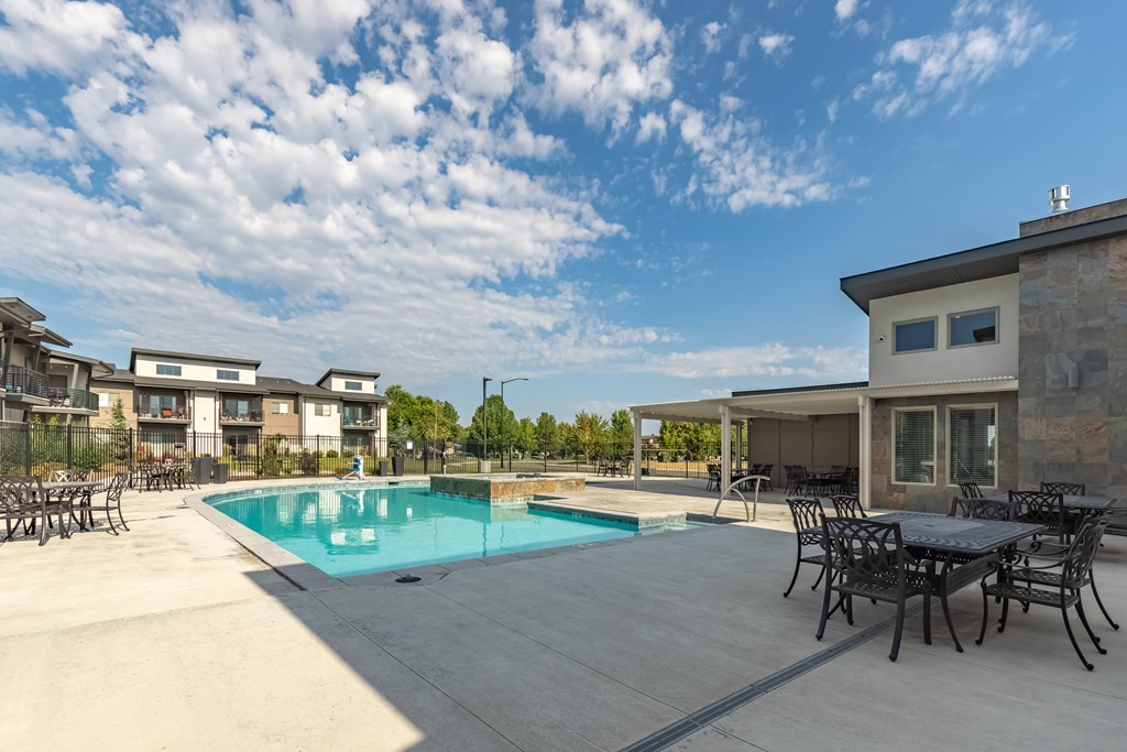 A swimming pool surrounded by a patio with chairs and a house in the background. at Harper Ridge Apartments, Idaho