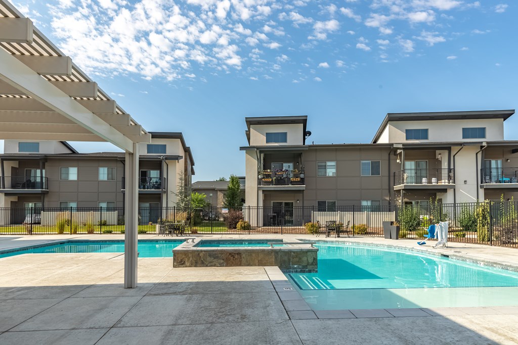 A swimming pool is surrounded by a concrete patio and a building with a balcony. at Harper Ridge Apartments, Meridian, 83642