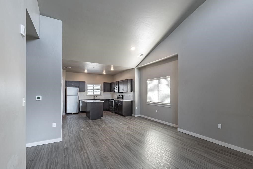 an empty living room with a kitchen in the background