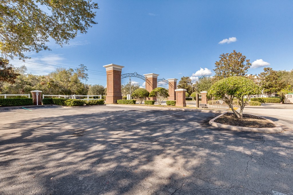 a parking lot in front of a park with trees and columns