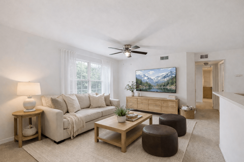 A living room with a white couch, a wooden coffee table, and a painting of a mountain landscape on the wall.