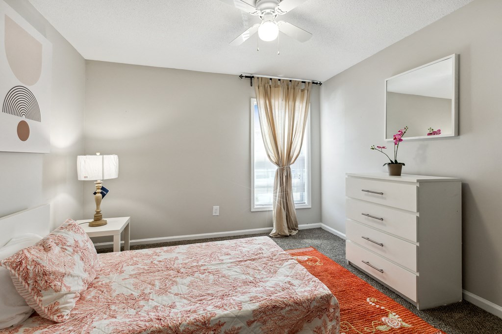 A bedroom with a bed, dresser, and window.