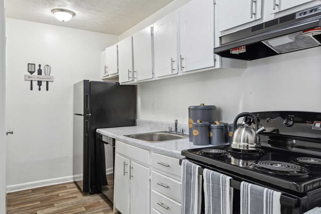 A black refrigerator is in a kitchen with white cabinets.