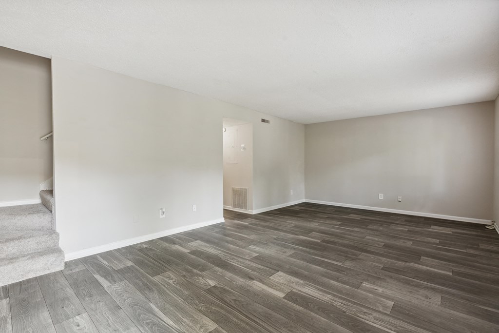 A room with a wooden floor and a staircase on the left side.