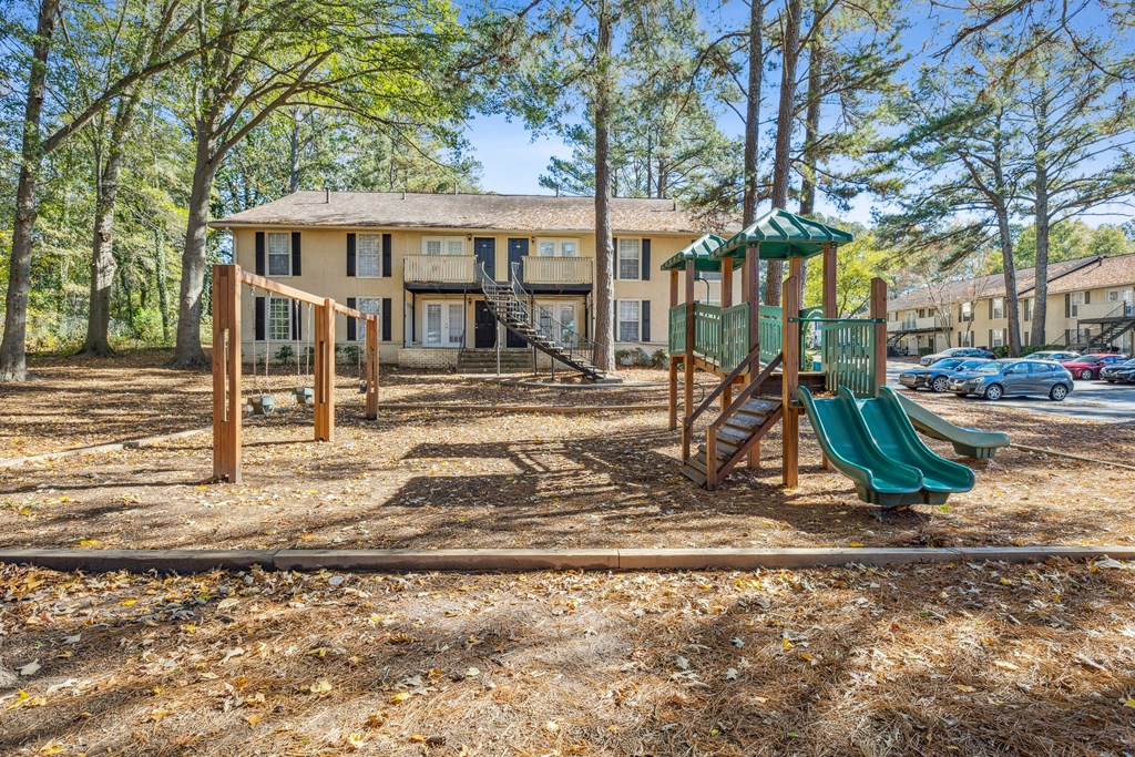 A playground with a green slide and a wooden swing set.