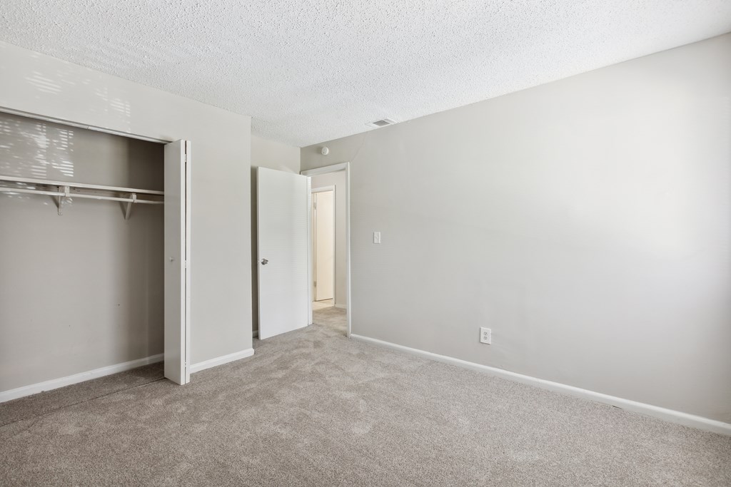 A room with a carpeted floor and a closet with a door open.