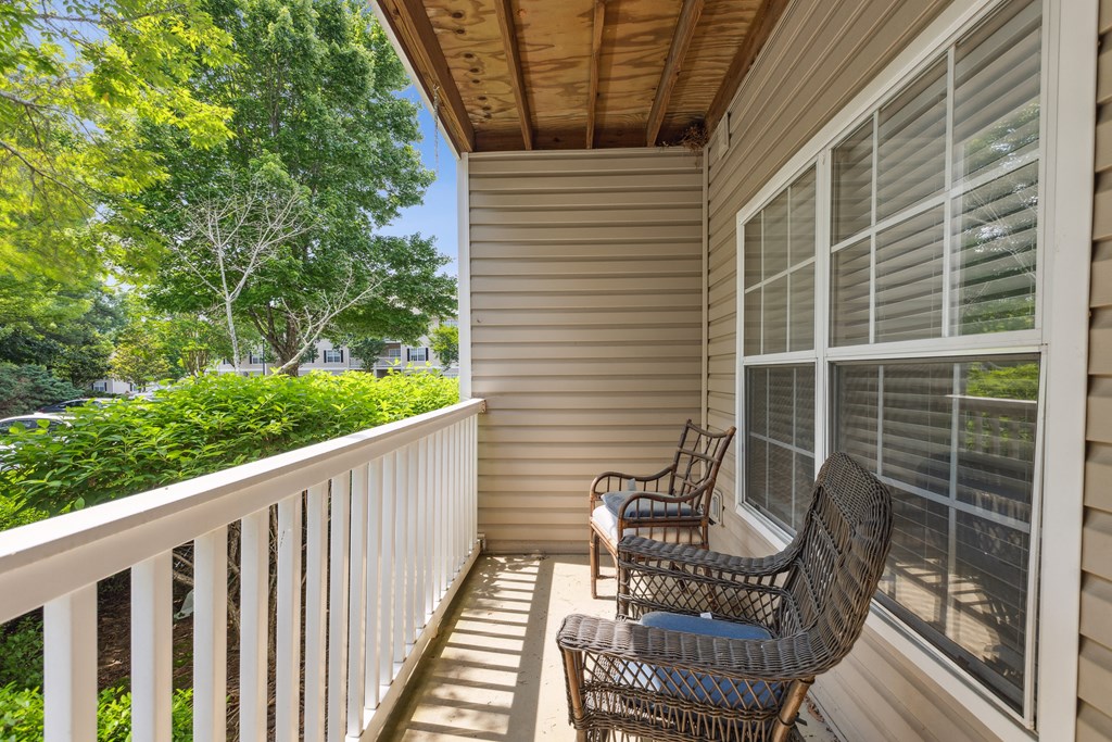 two wicker chairs on a porch with a view of the yard and trees