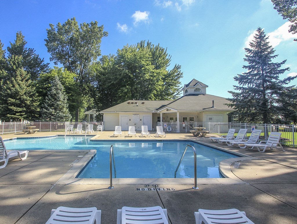 a swimming pool with chairs and a house in the background
