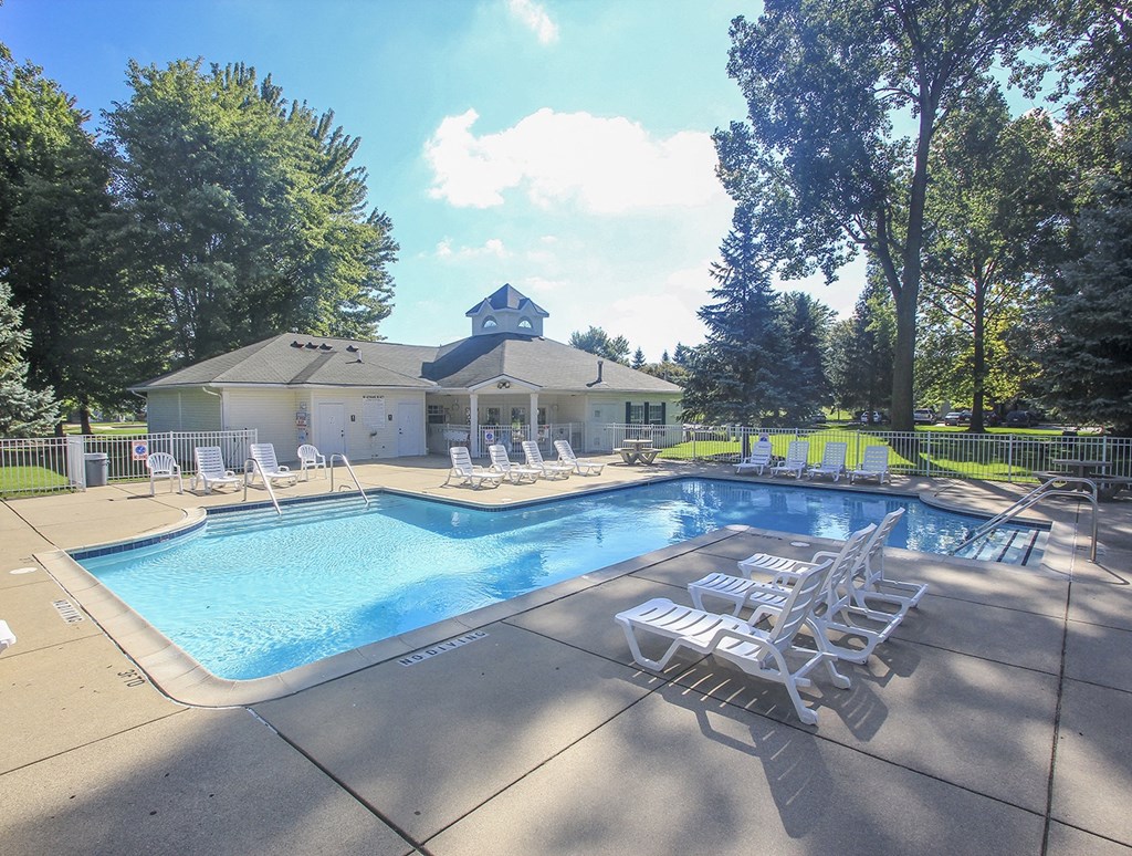 a swimming pool with chairs and a house in the background