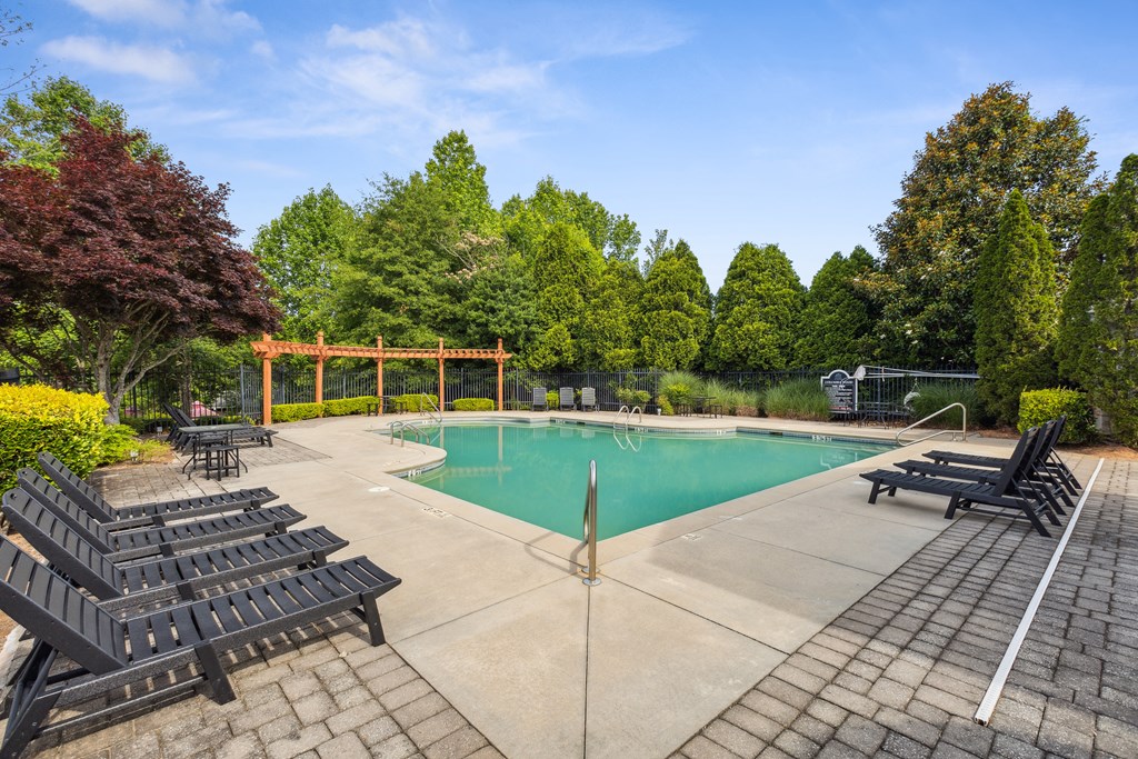 a swimming pool with black chairs and a fence and trees