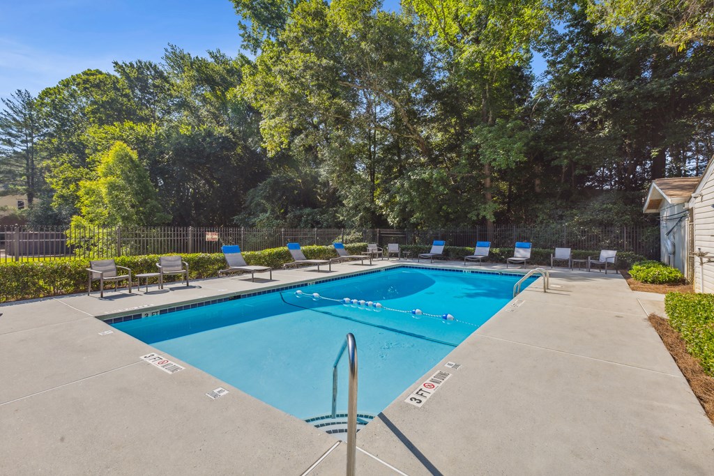 A swimming pool surrounded by trees and chairs.
