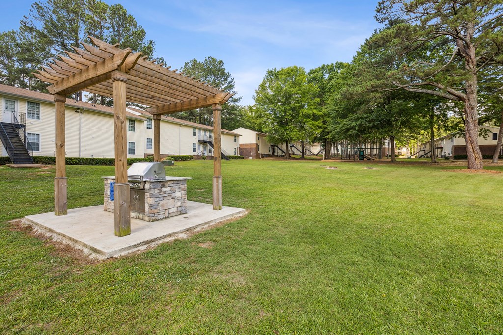 A wooden pergola is over a stone fireplace in a grassy area.