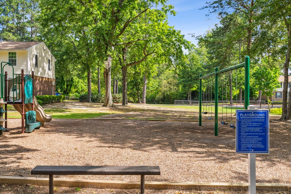 A playground with a sign that says "PLAYGROUND" in the middle of a wooded area.