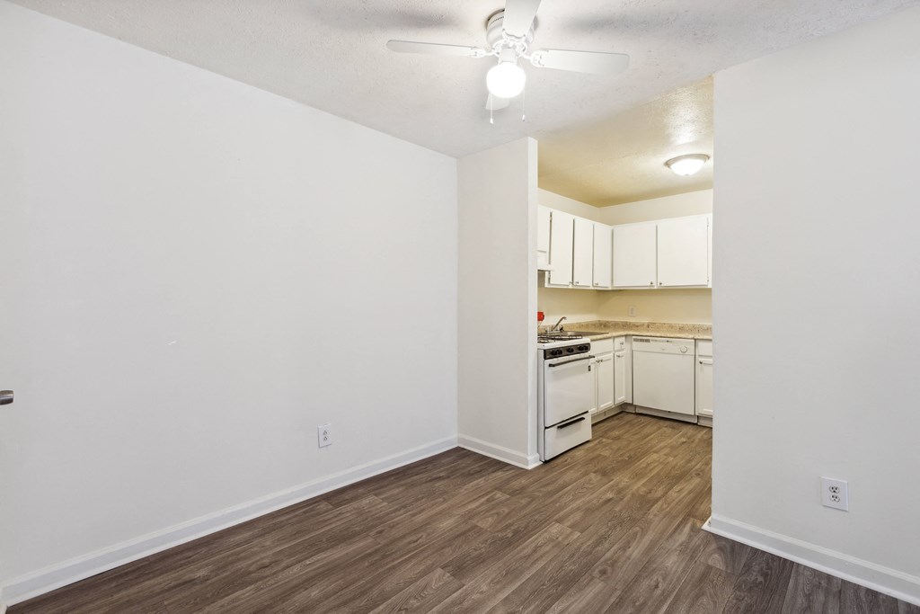 the living room and kitchen of an apartment with white walls and wood flooring