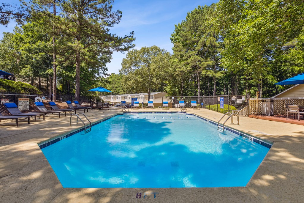 our resort style swimming pool is surrounded by chairs and trees