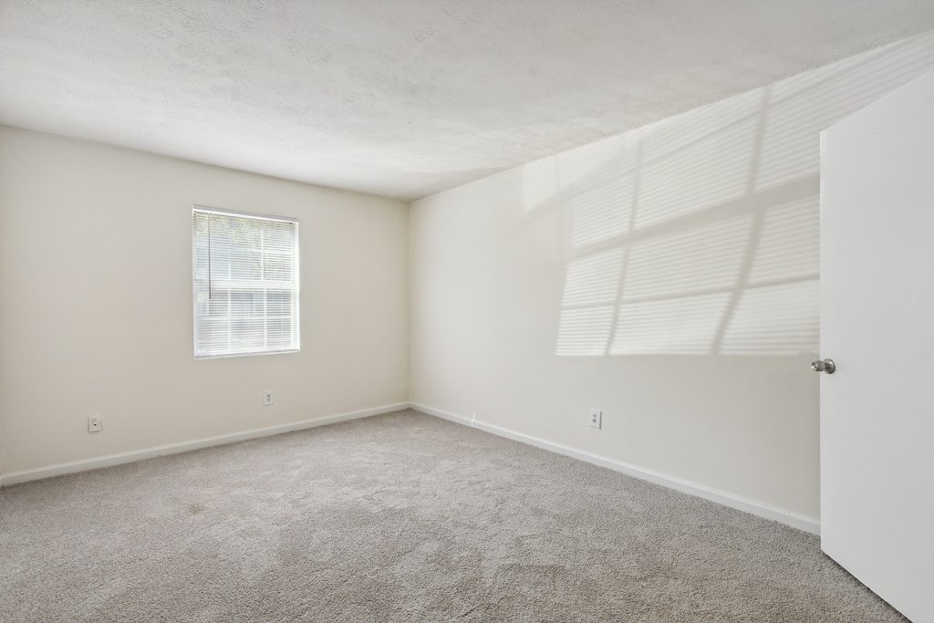 an empty bedroom with white walls and carpet and a window