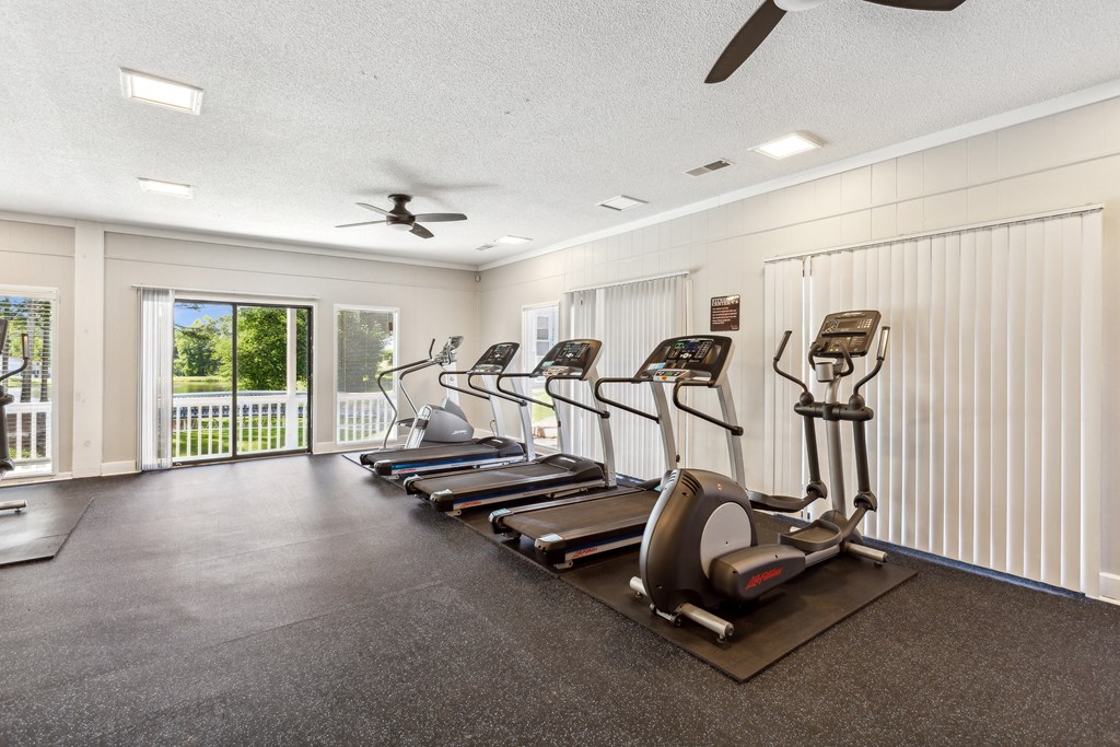 a gym with cardio machines and a ceiling fan