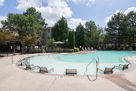A large swimming pool surrounded by trees and chairs.