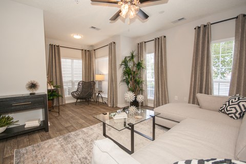A living room with a white couch, a glass coffee table, and a ceiling fan.