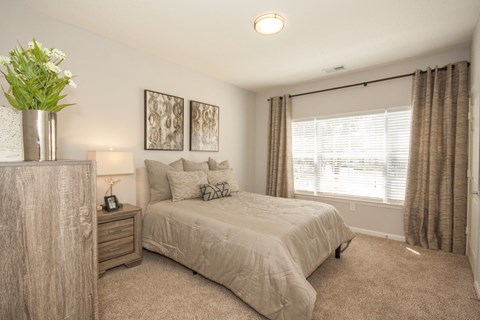 A bedroom with a bed, nightstand, and a plant.