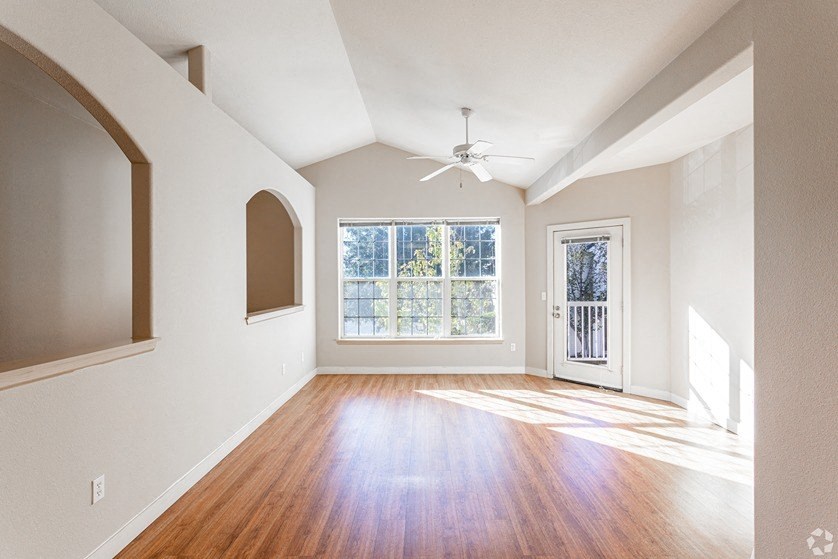 an empty living room with a window and a ceiling fan