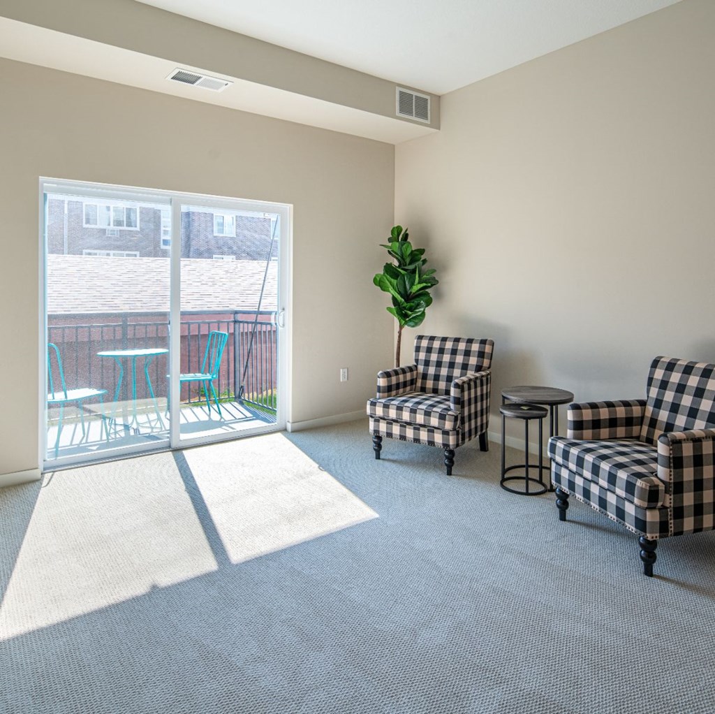 a living room with chairs and a sliding glass door to a balcony
