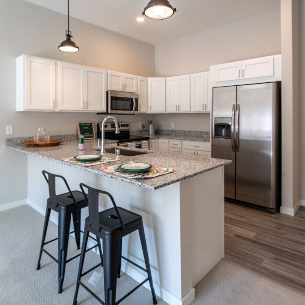 a kitchen with bar stools and stainless steel refrigerator
