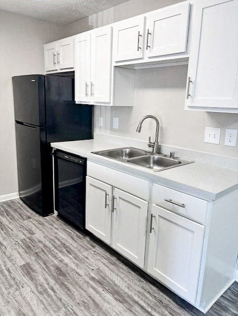 A black refrigerator is in a kitchen with white cabinets.