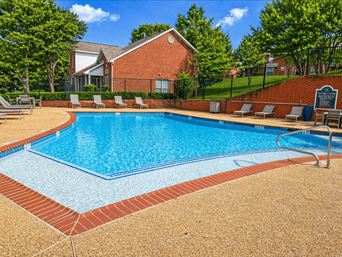 A pool surrounded by a brick border and lounge chairs.