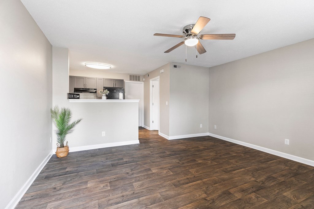 an empty living room with a ceiling fan and a kitchen