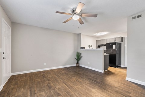 an empty living room with a ceiling fan and a kitchen