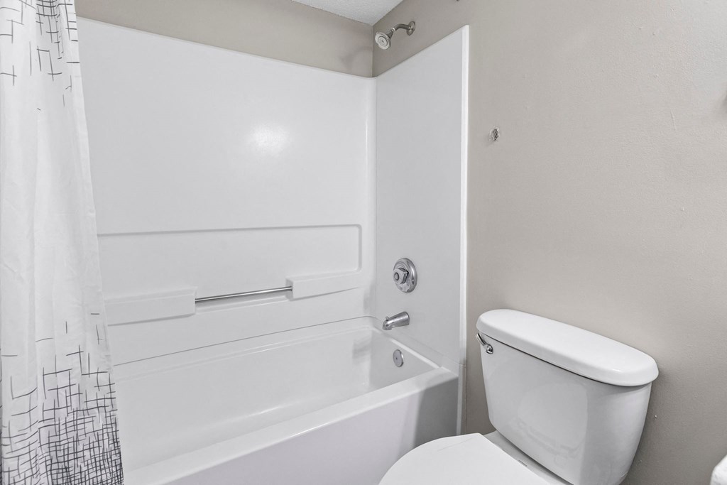 A white bathroom with a toilet, bathtub, and shower curtain.
