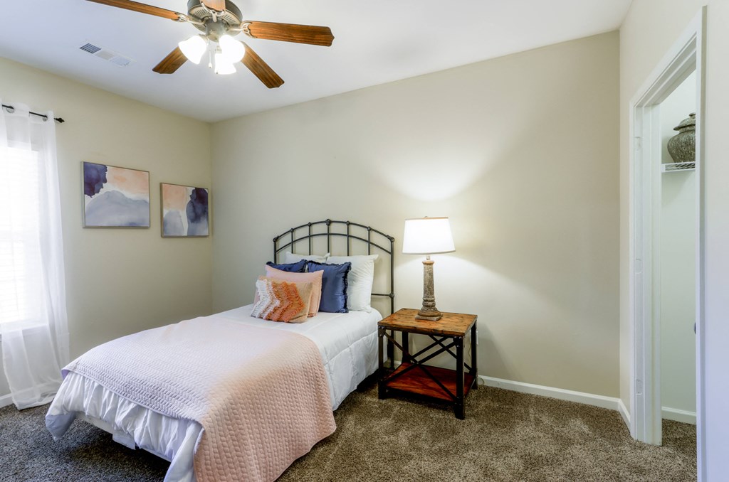 A bedroom with a bed, a table with a lamp, and two pictures on the wall.